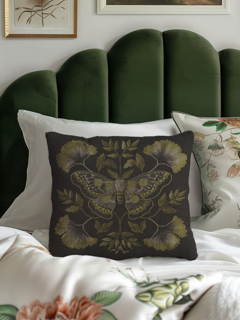 A square decorative pillow featuring an intricately detailed Luna moth in sage green and olive tones on a black background. The moth is centered in a symmetrical arrangement with ginkgo-like leaves and botanical elements surrounding it.